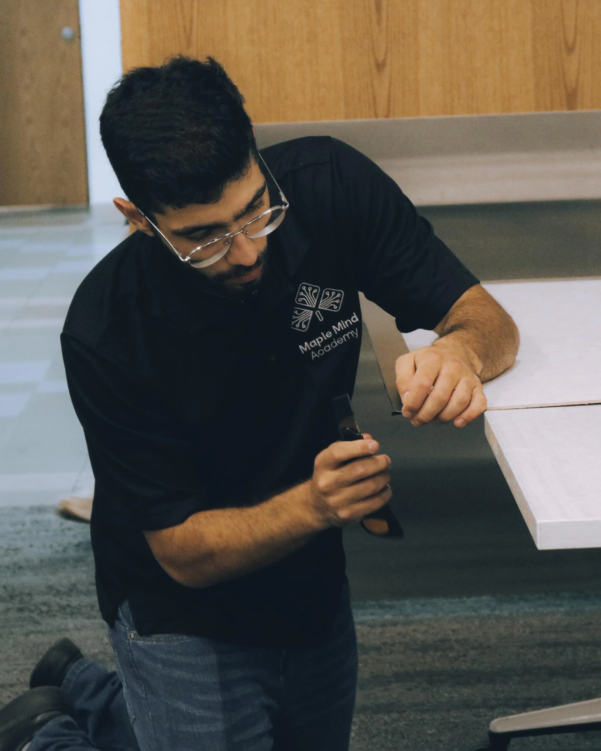 Instructor kneeling beside a table to adjust a small part in a classroom