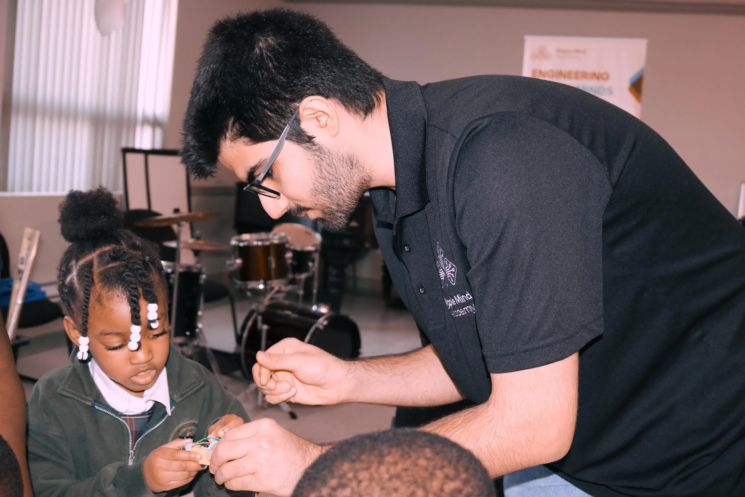 Instructor helping a young girl in a school uniform connect a small electronic part