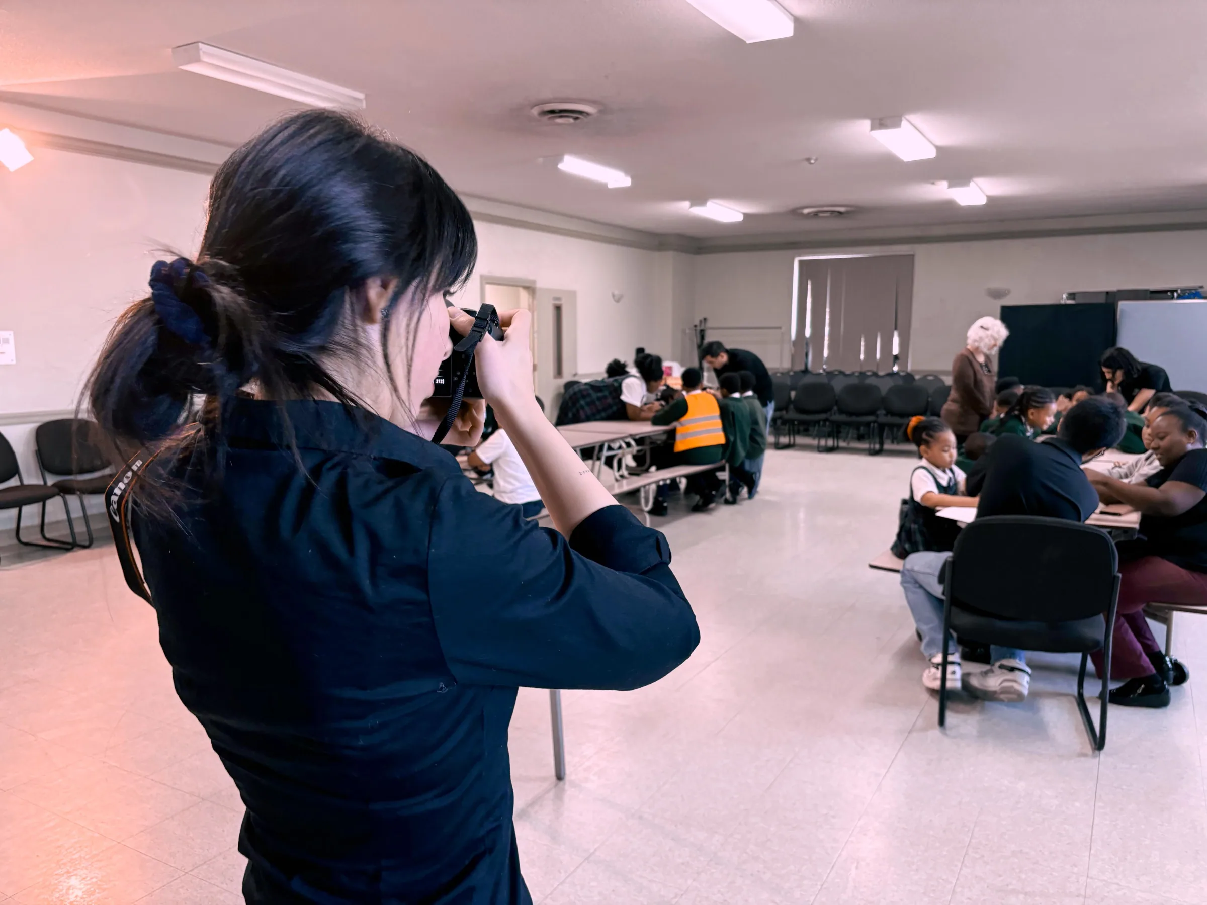 Instructor photographing children working at tables in a large hall