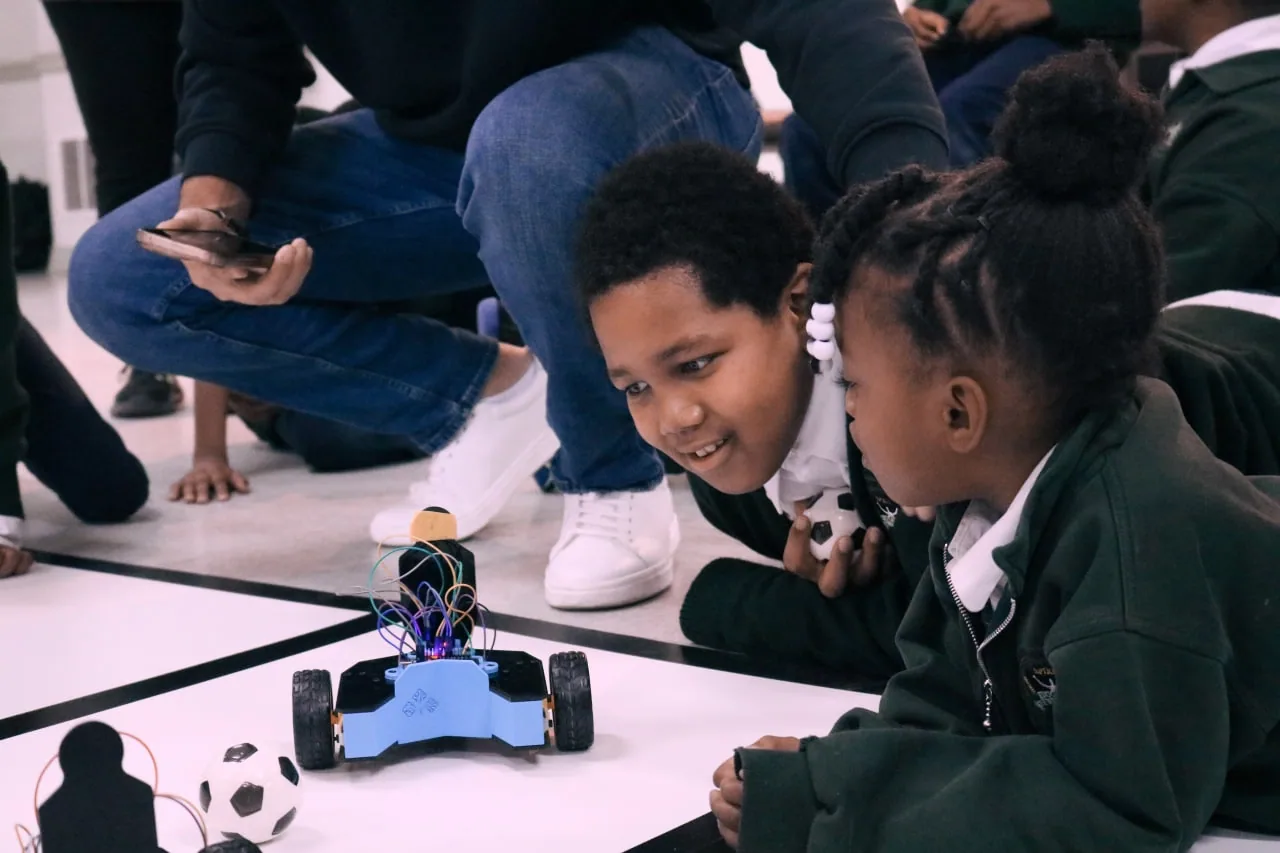 Spectators watching robots compete on a marked arena floor